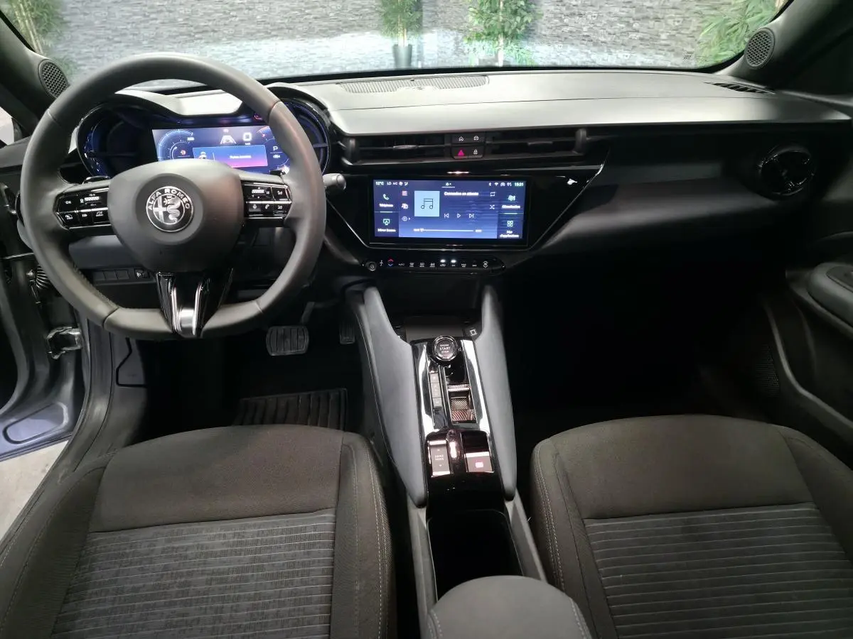 Vue intérieure avant de l'Alfa Romeo Junior 1.2 Ibrida 2025, tableau de bord moderne avec écran tactile et volant multifonctions.