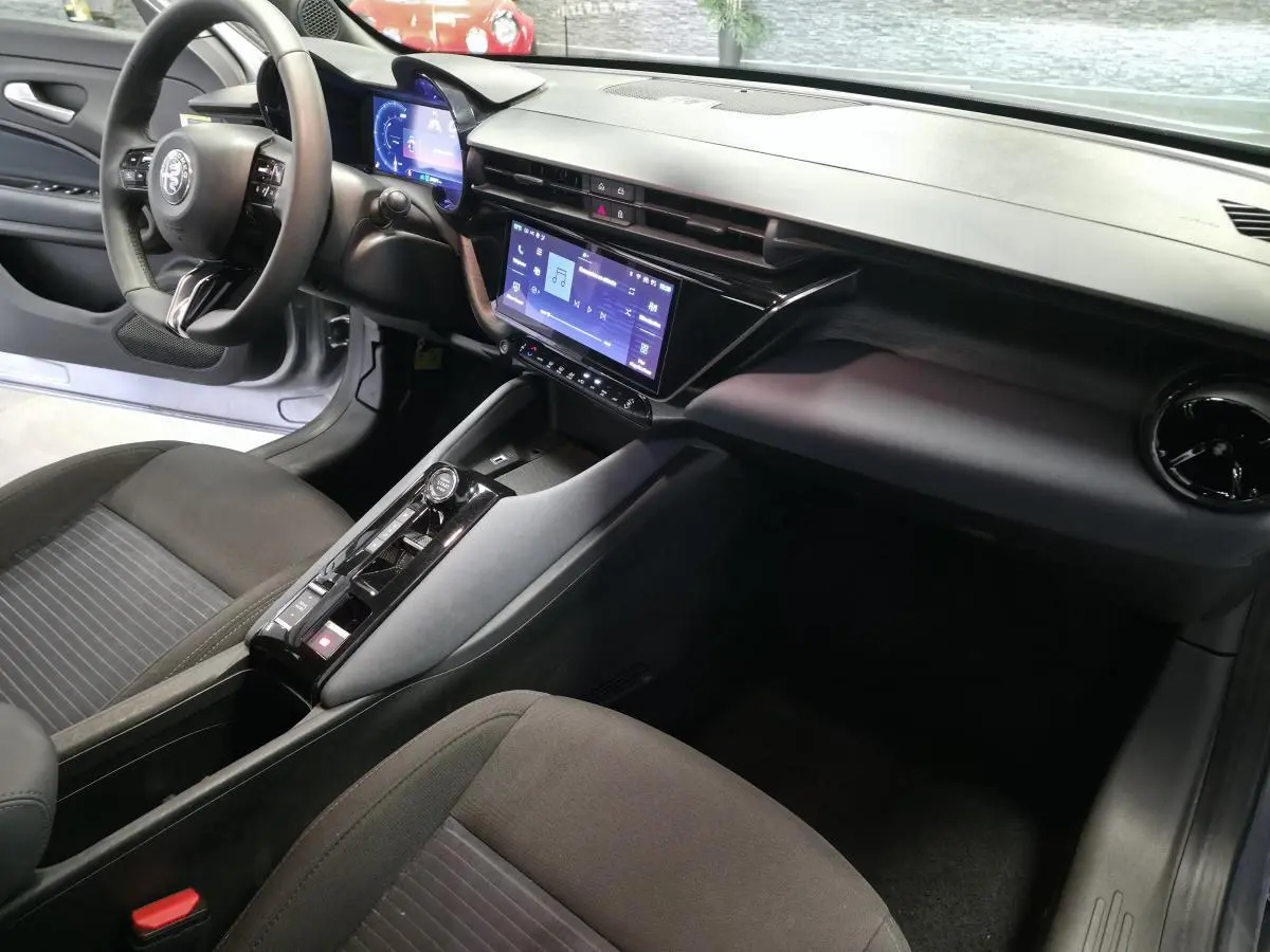 Intérieur de l'Alfa Romeo Junior 1.2 Ibrida 2025 vu côté conducteur, tableau de bord moderne avec écran tactile.