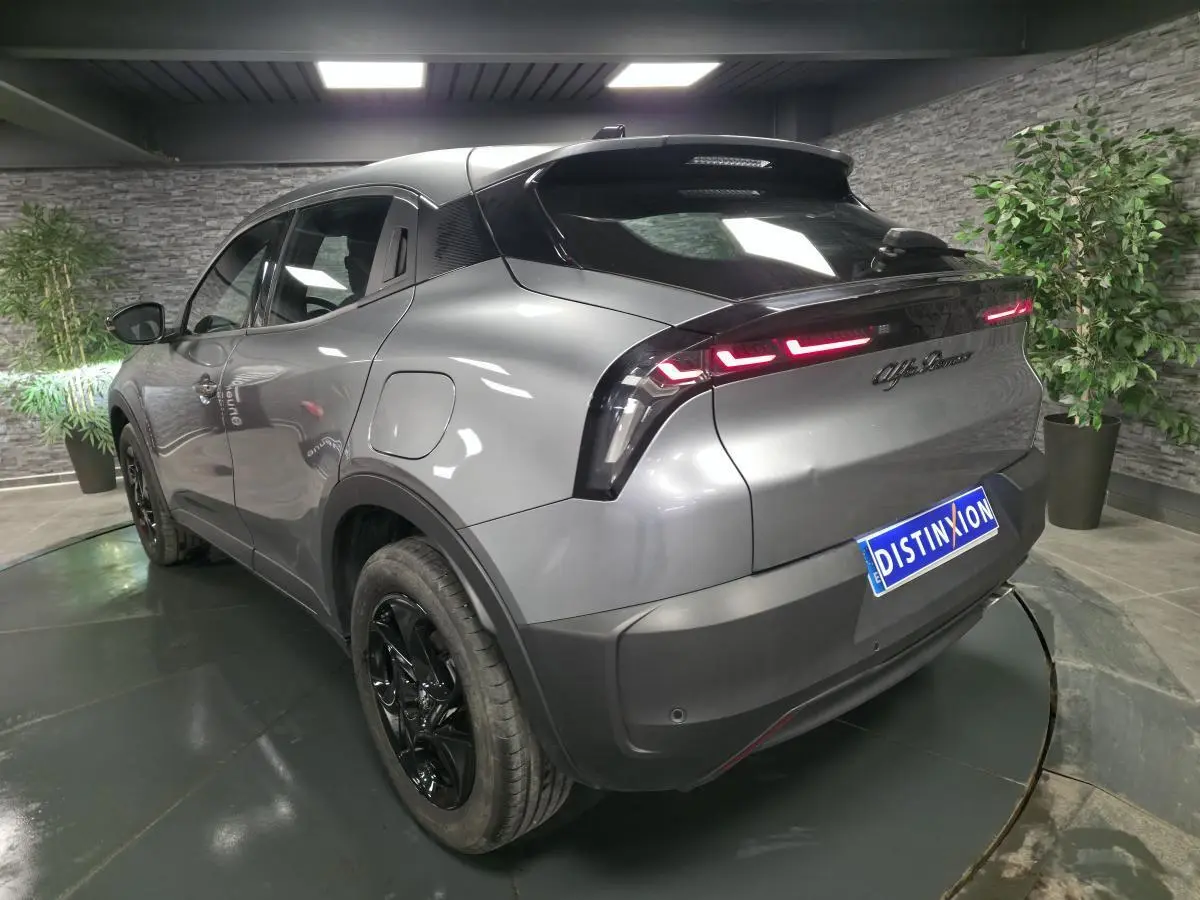 Vue 3/4 arrière gauche de l'Alfa Romeo Junior gris métallisé avec feux arrière LED et jantes noires brillantes.