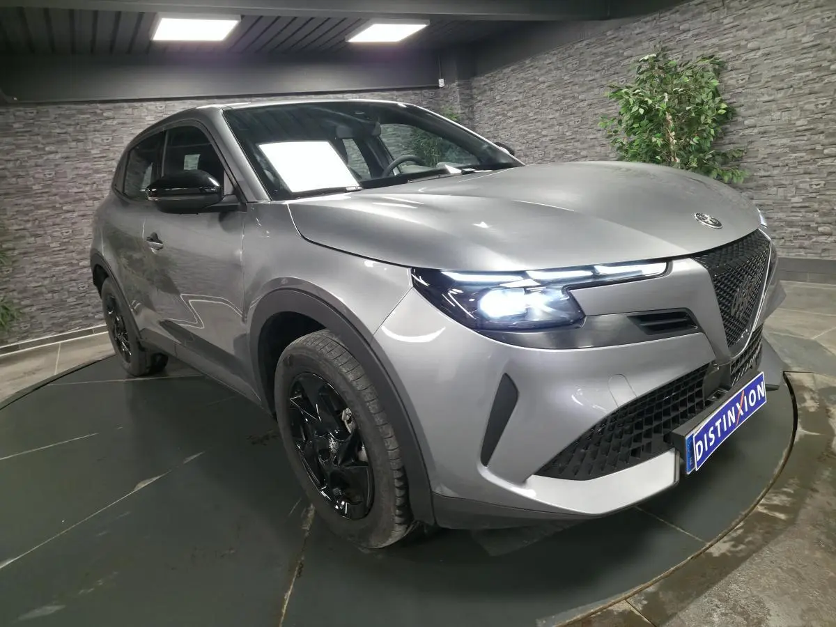 Vue 3/4 avant droite de l'Alfa Romeo Junior 1.2 hybride gris métallisé avec jantes noires et phares LED allumés.