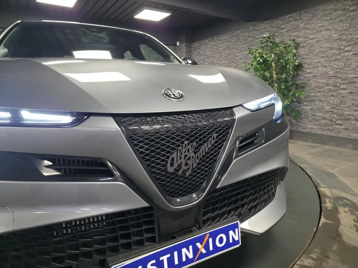 Vue avant rapprochée de l'Alfa Romeo Junior 1.2 hybride gris métallisé avec calandre noire et phares LED allumés.