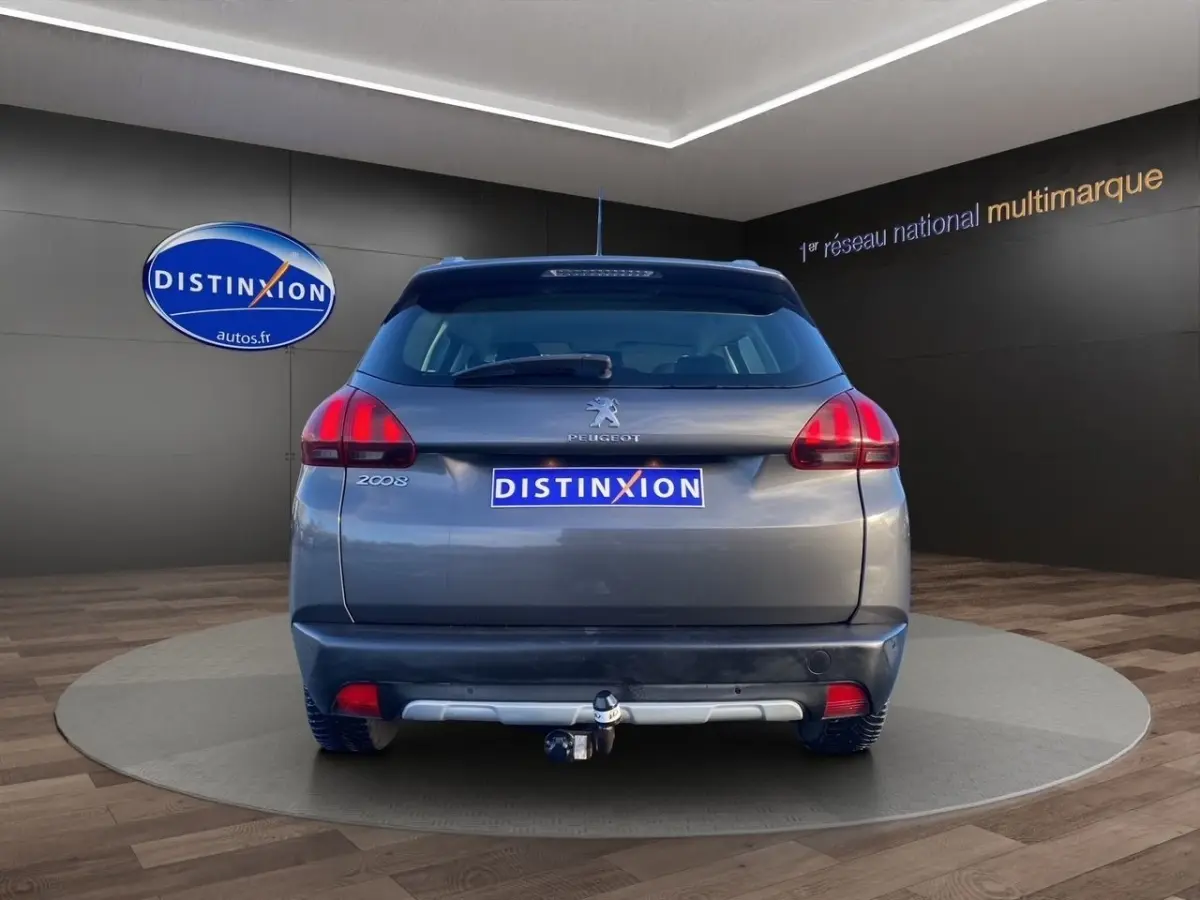 Vue arrière d’un Peugeot 2008 gris foncé avec spoiler de toit et attelage de remorque visible en intérieur showroom.