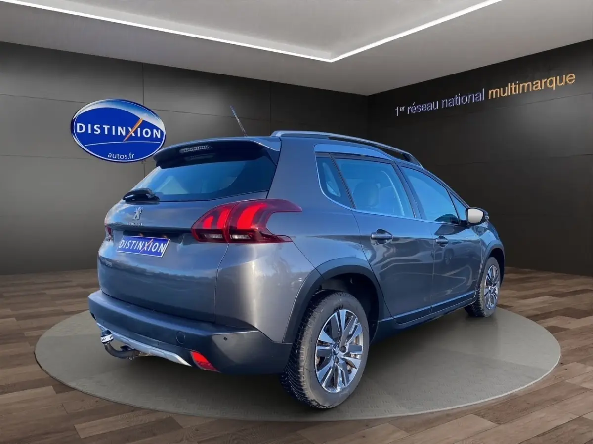 Peugeot 2008 gris foncé vue 3/4 arrière droit, avec spoiler de toit et jantes alliage visibles.