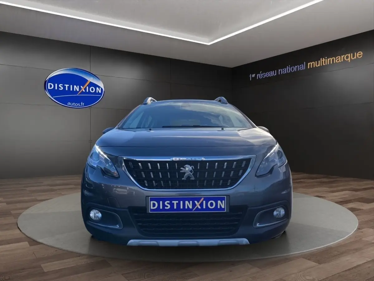 Vue frontale d'un Peugeot 2008 gris foncé avec calandre distinctive et feux LED dans un showroom.