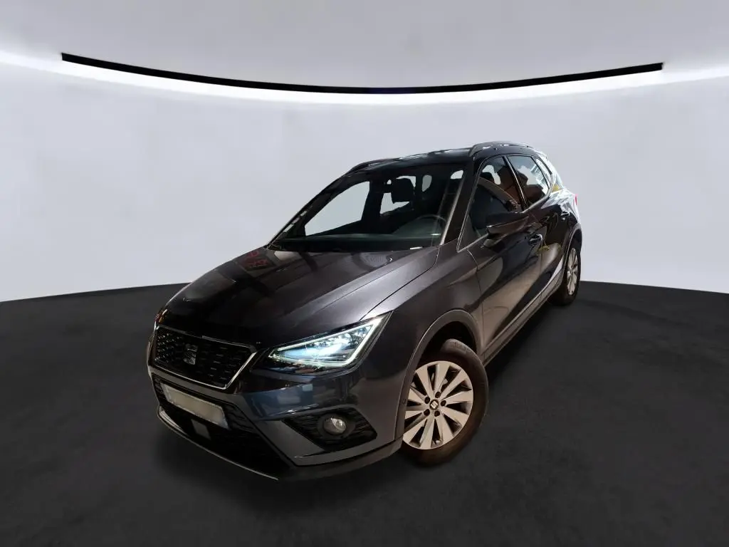 SEAT Arona gris foncé vue 3/4 avant droit, phares allumés et jantes alliage, dans un studio lumineux.