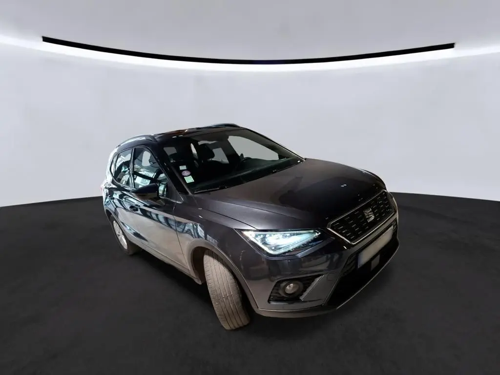 SEAT Arona gris foncé en 3/4 avant droit, phares allumés, sur fond neutre en studio.