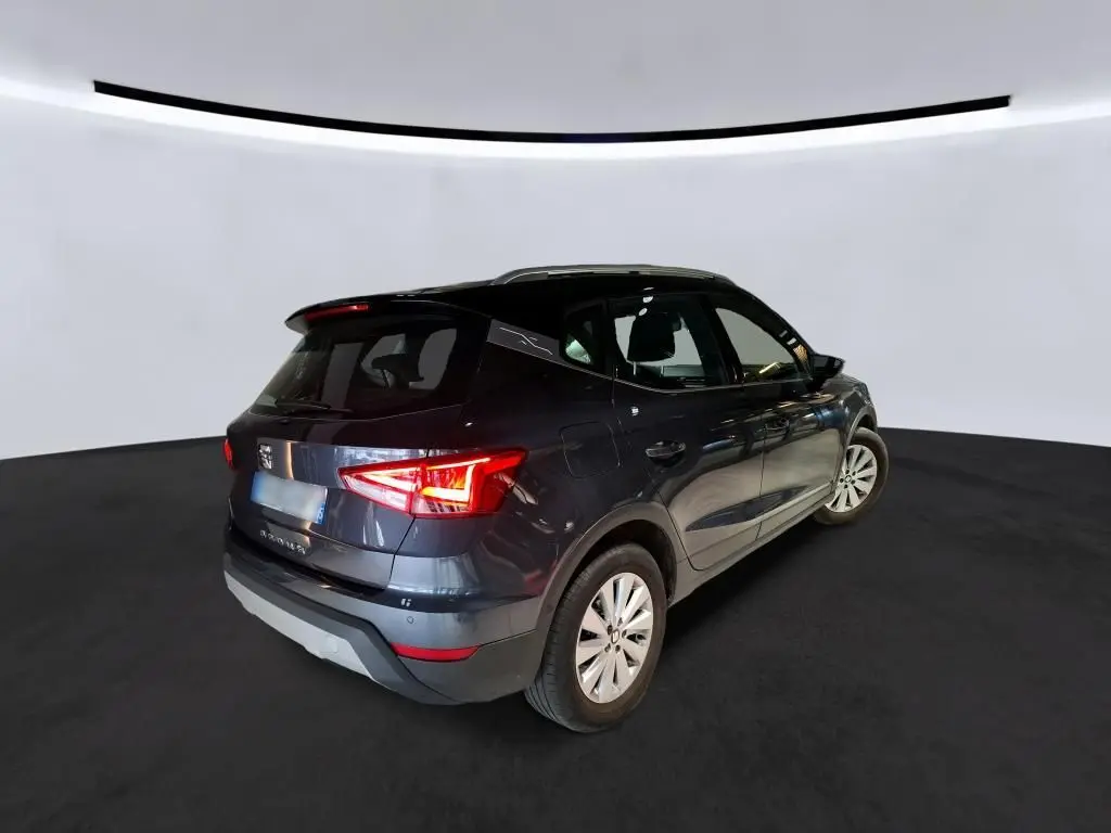 SEAT Arona gris foncé vue 3/4 arrière droit, avec feux arrière allumés et jantes argentées, sur fond neutre.