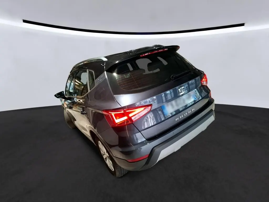 Vue 3/4 arrière droite d'un SEAT Arona gris foncé avec feux arrière allumés dans un studio lumineux.