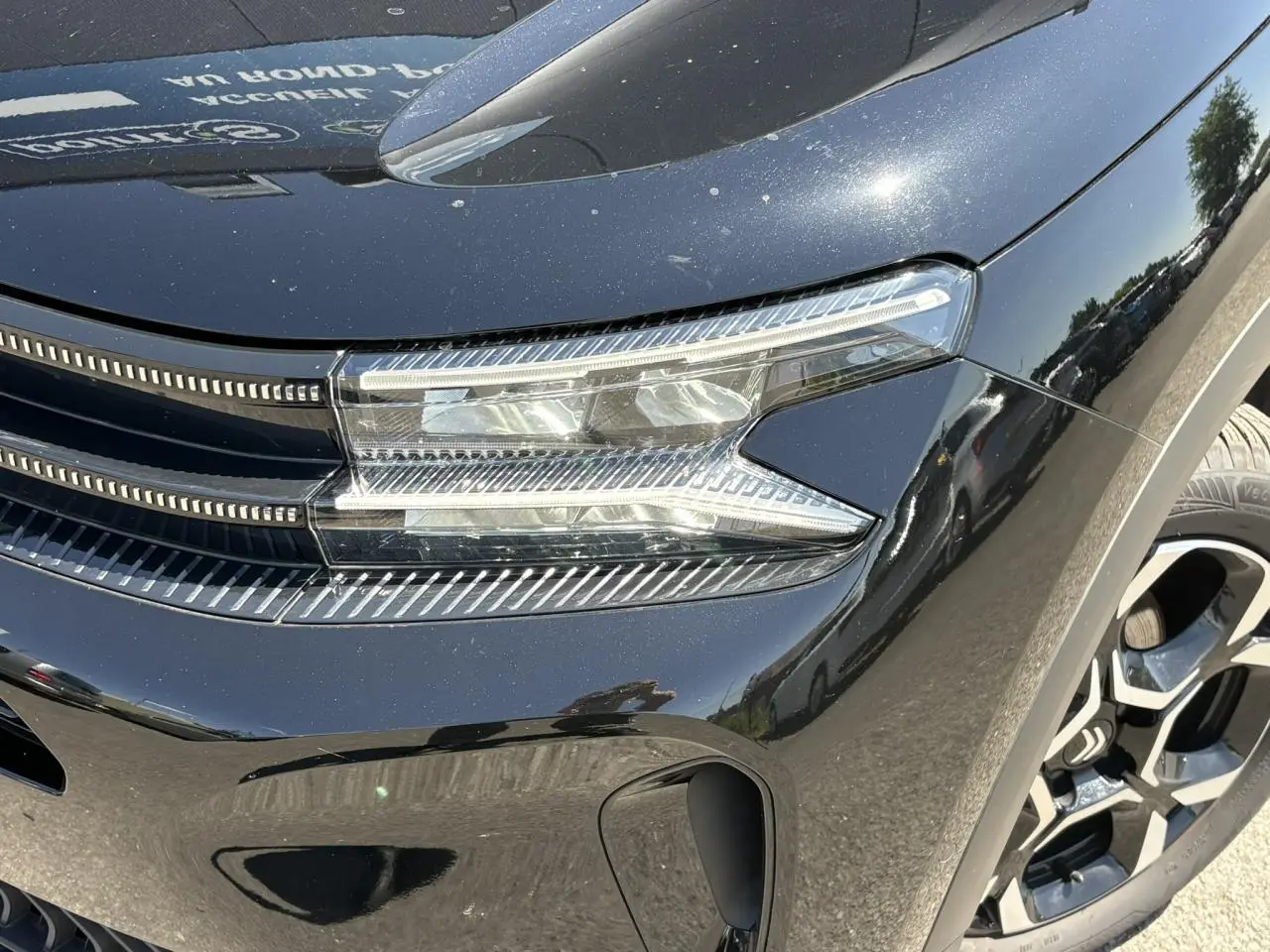 Gros plan sur le phare avant droit du Citroën C5 Aircross Hybrid noir Perla avec jante alliage visible.