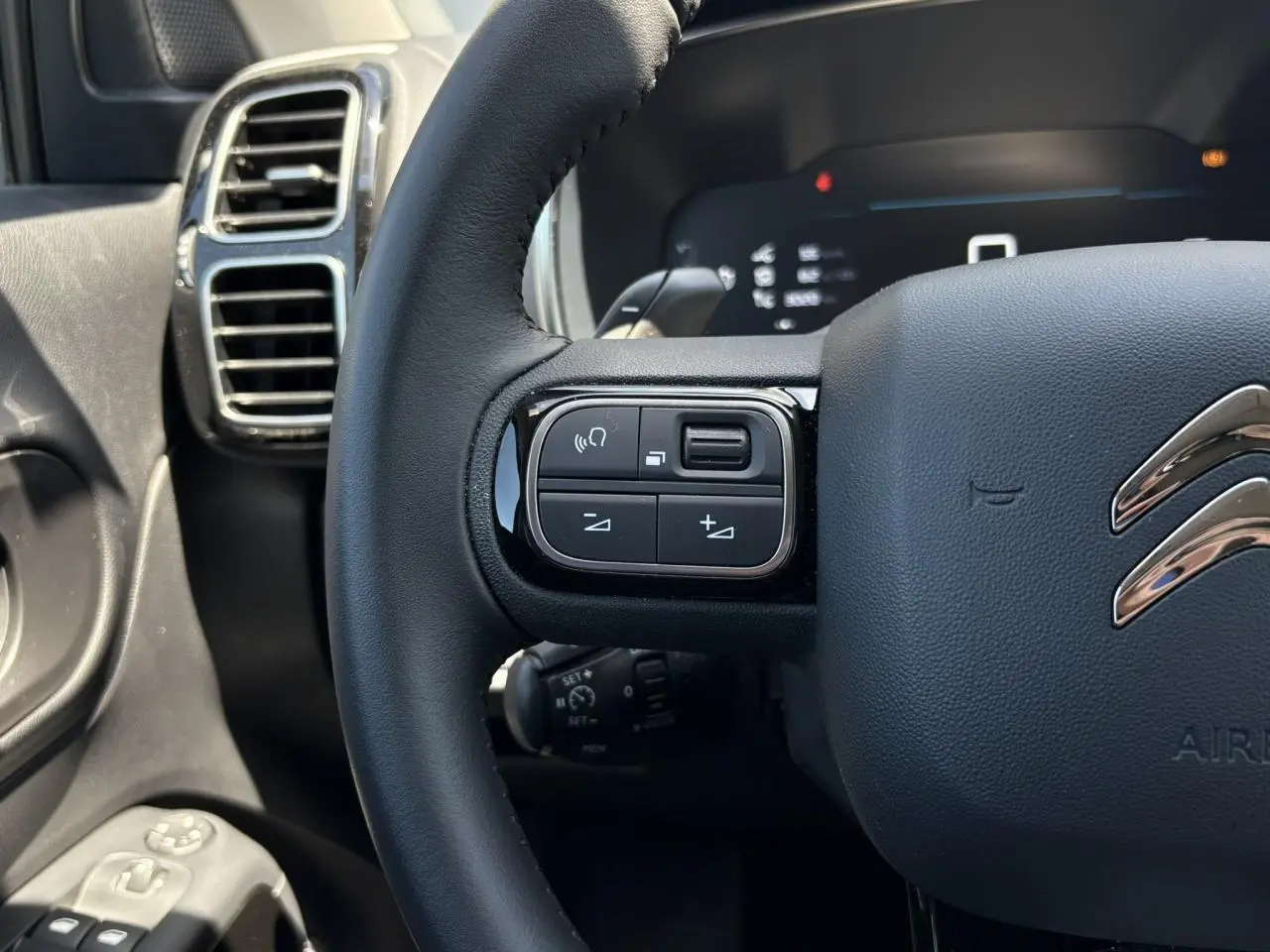 Gros plan sur le volant noir du Citroën C5 Aircross Hybrid 2025, avec commandes intégrées et aérateurs chromés en arrière-plan.