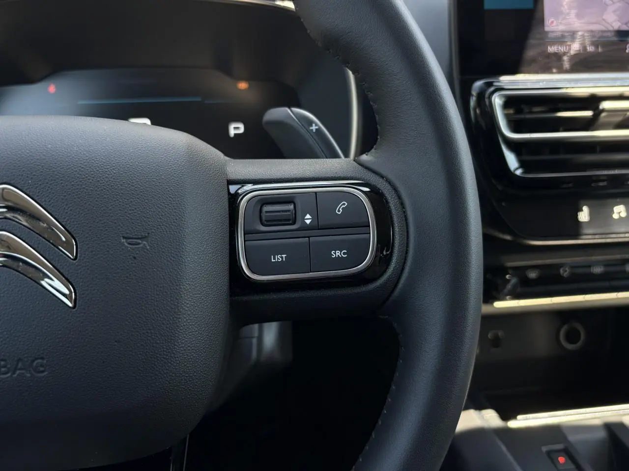 Gros plan sur le volant noir du Citroën C5 Aircross Hybrid 2025, avec commandes intégrées et palettes au volant visibles.