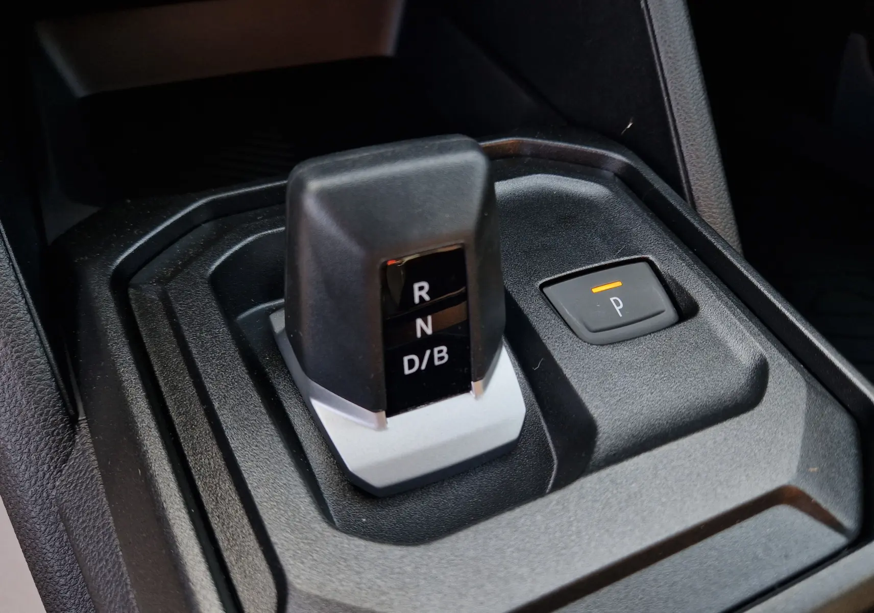 Gros plan sur le levier de vitesses automatique noir et gris du Dacia Duster blanc 2026 avec bouton de parking éclairé.