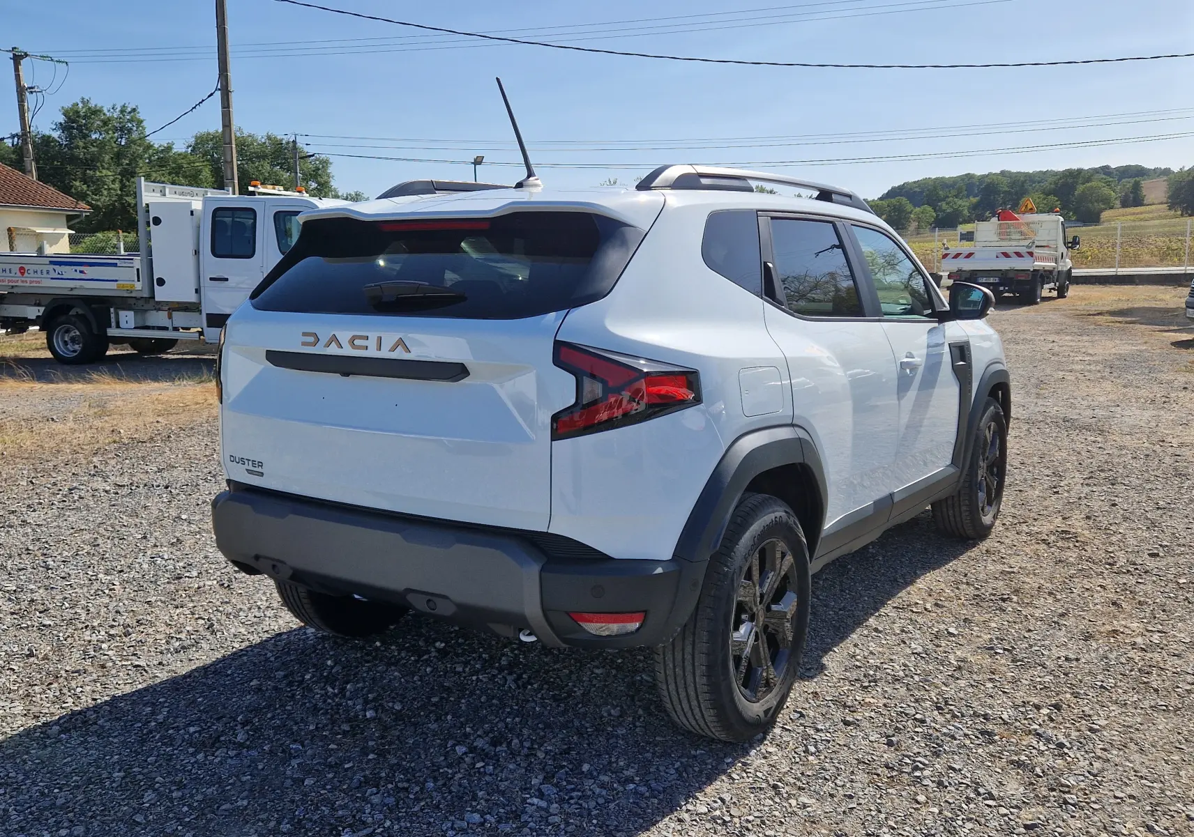 Vue 3/4 arrière droite d'un Dacia Duster blanc 2026 avec jantes noires et détails noirs contrastants.
