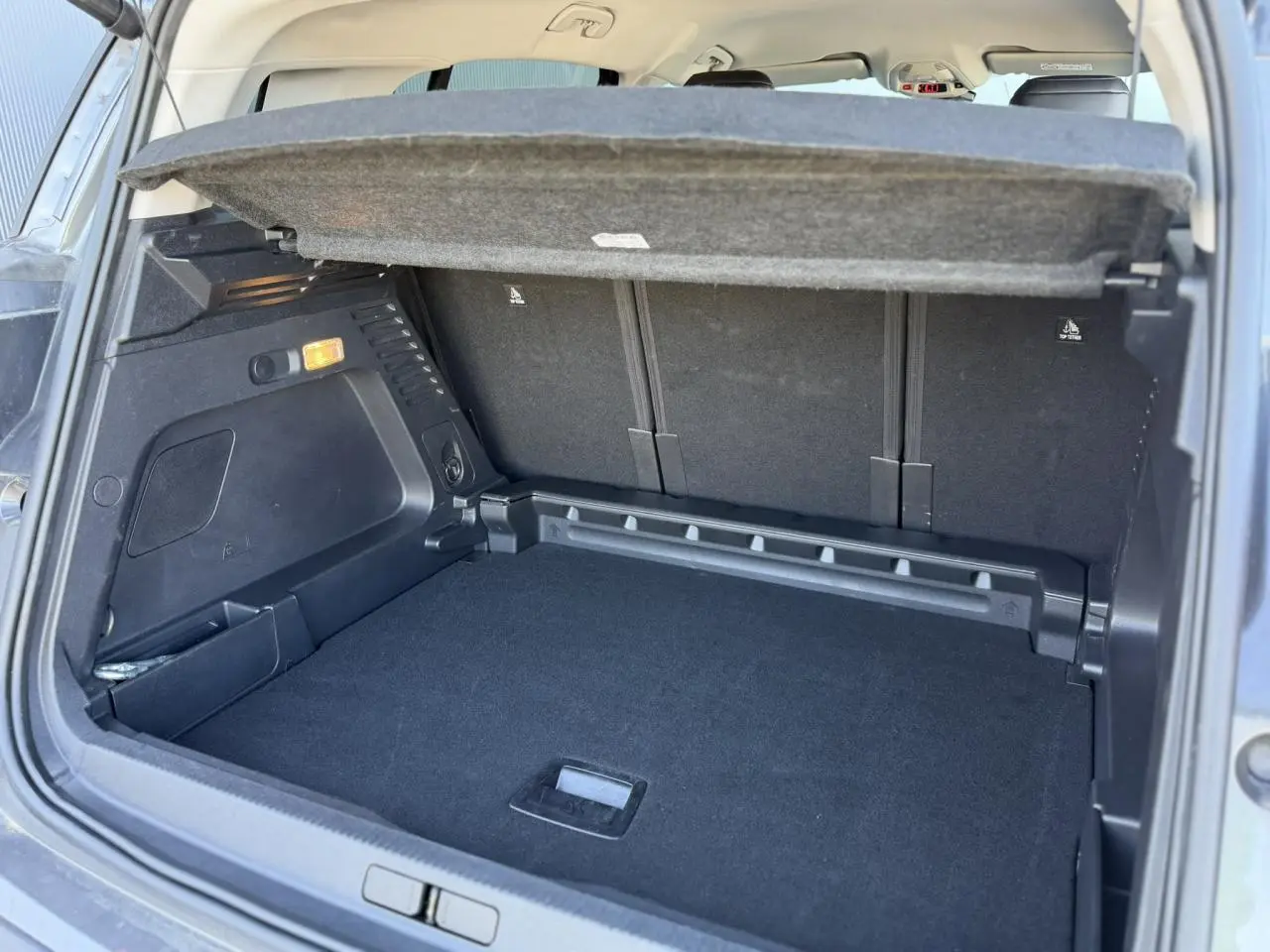 Vue intérieure du coffre ouvert du Citroën C5 Aircross Hybrid gris Platinium, montrant le plancher modulable et la tablette arrière.