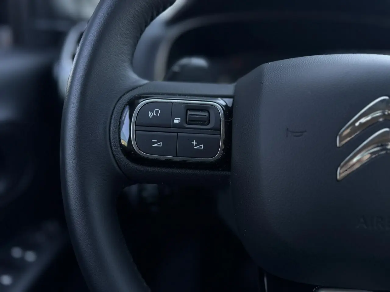 Gros plan sur les commandes gauche du volant noir du Citroën C5 Aircross Hybrid gris Platinium, intérieur moderne.