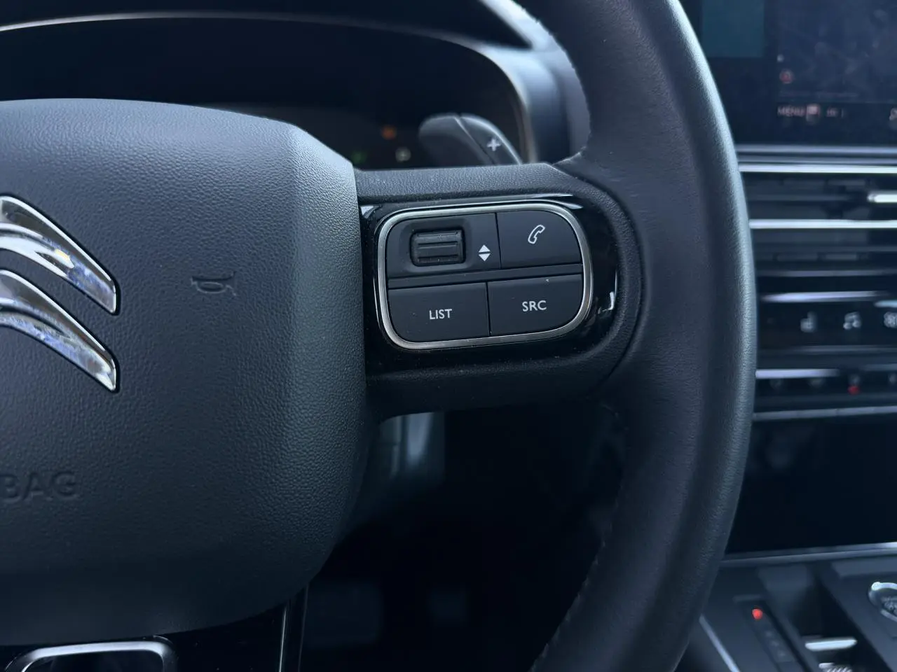 Gros plan sur les commandes gauche du volant cuir noir du Citroën C5 Aircross Hybrid 2025, avec tableau de bord en arrière-plan.