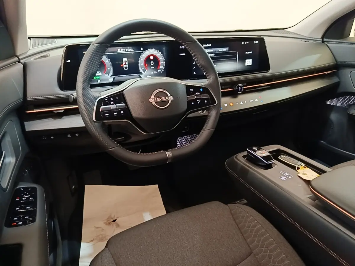 Vue intérieure avant du Nissan Ariya noir 2026, volant cuir multifonctions et grand écran tactile panoramique.