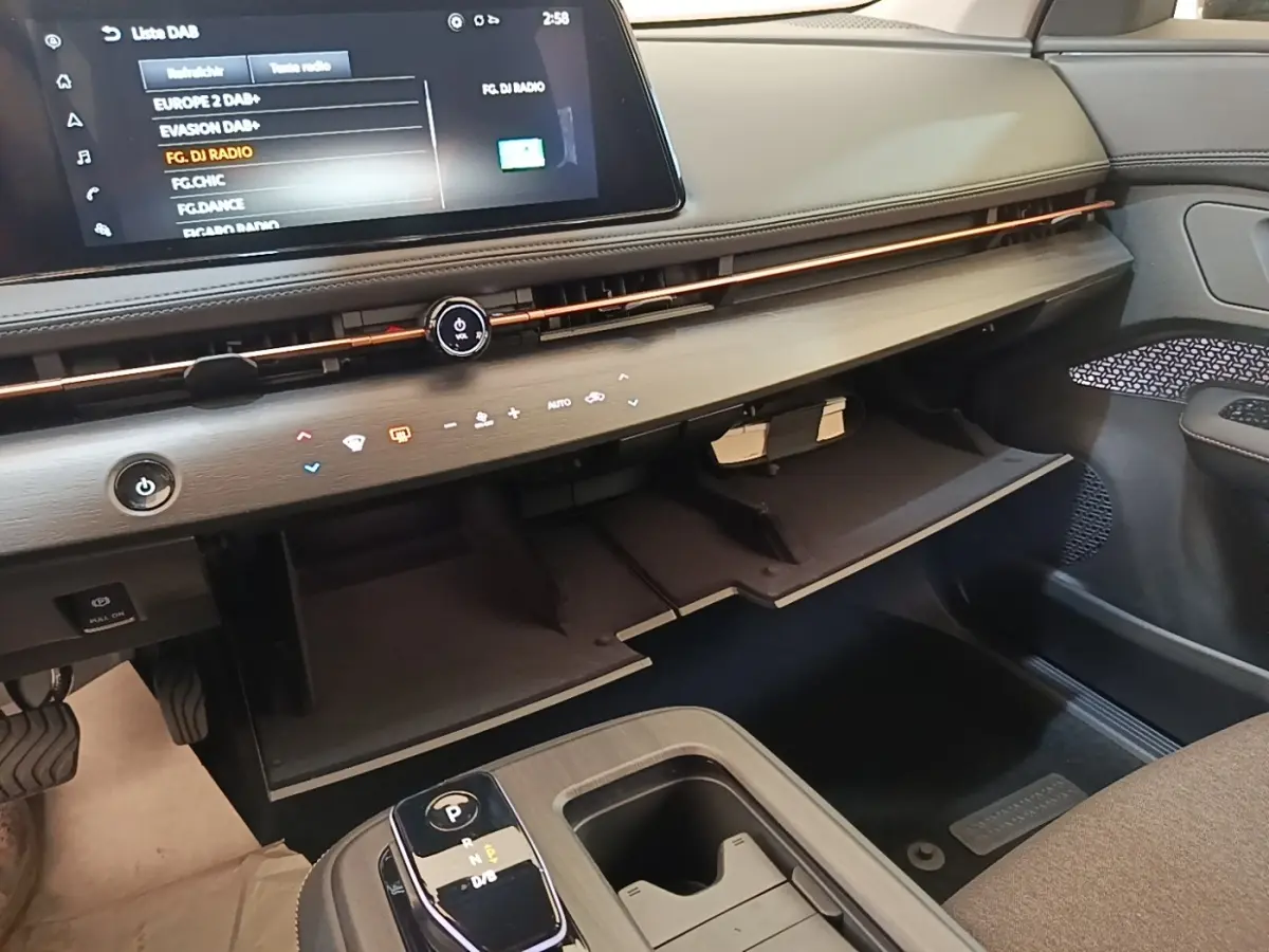 Intérieur du Nissan Ariya 63kWh noir, vue côté passager sur tableau de bord avec boîte à gants ouverte et écran tactile.