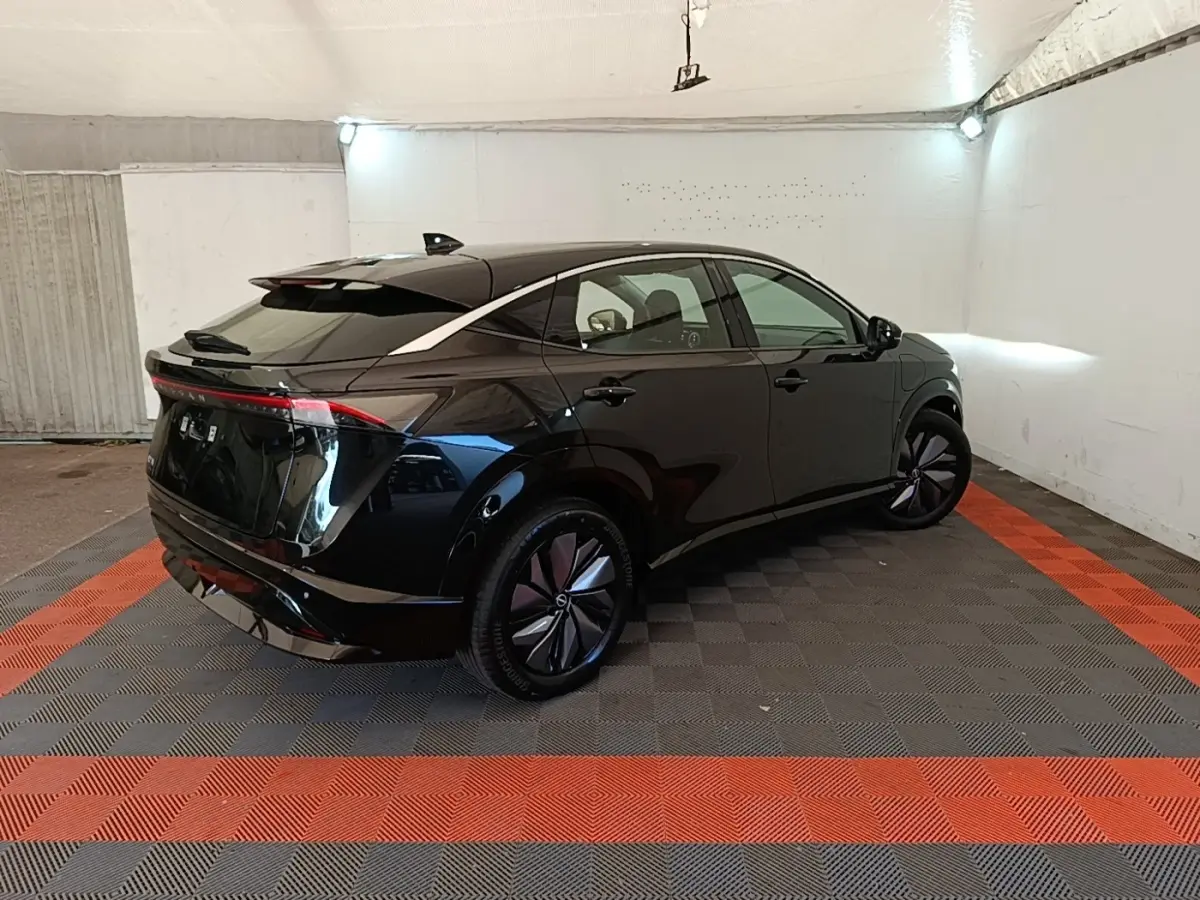 Nissan Ariya 63kWh noir en 3/4 arrière droit, avec feux arrière LED et jantes aérodynamiques dans un garage.