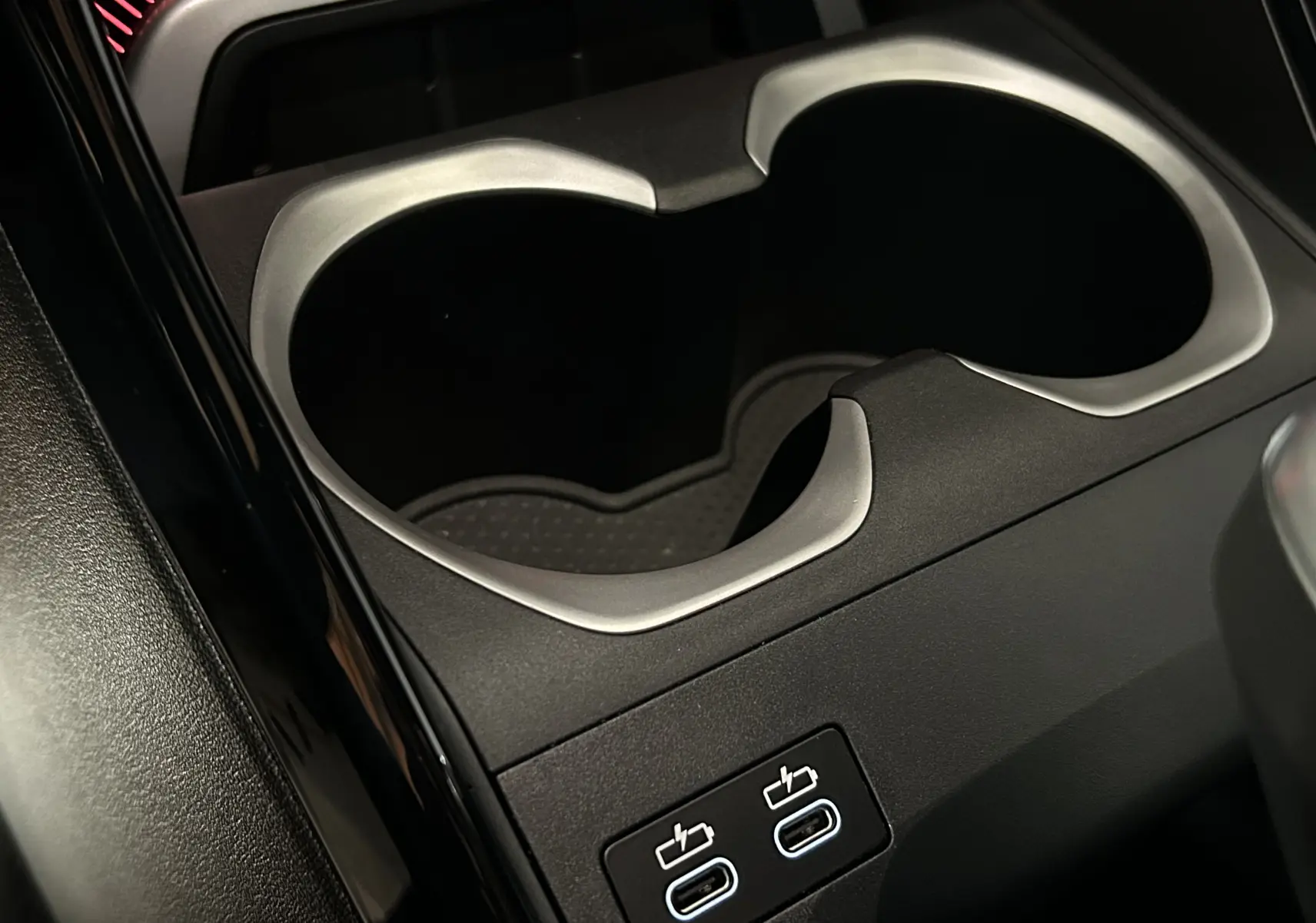 Gros plan sur la console centrale noire du BMW X1 2024 avec porte-gobelets et deux ports USB-C lumineux.