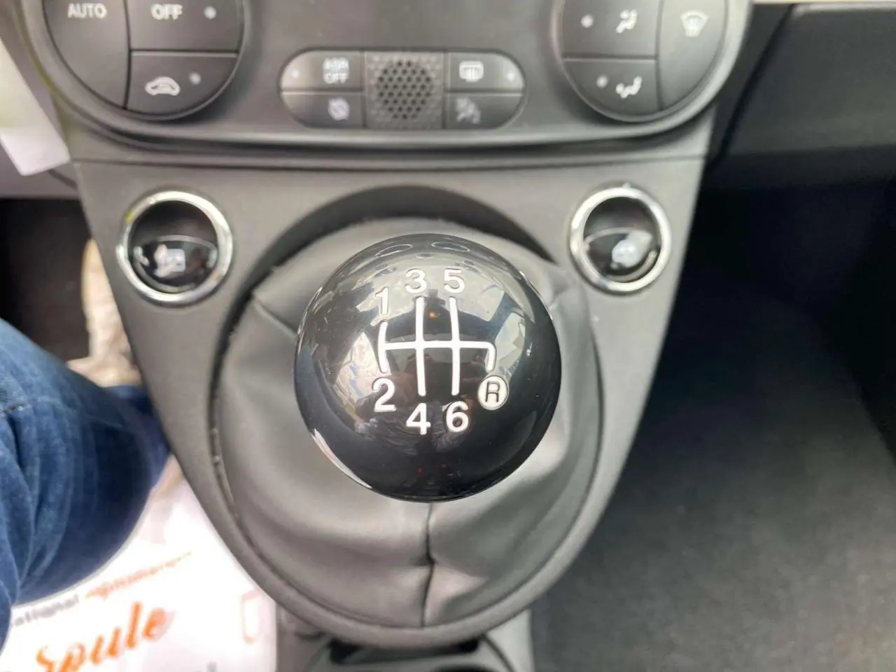 Gros plan sur le levier de vitesses manuel noir de la FIAT 500 2024, avec commandes climatisation en arrière-plan.