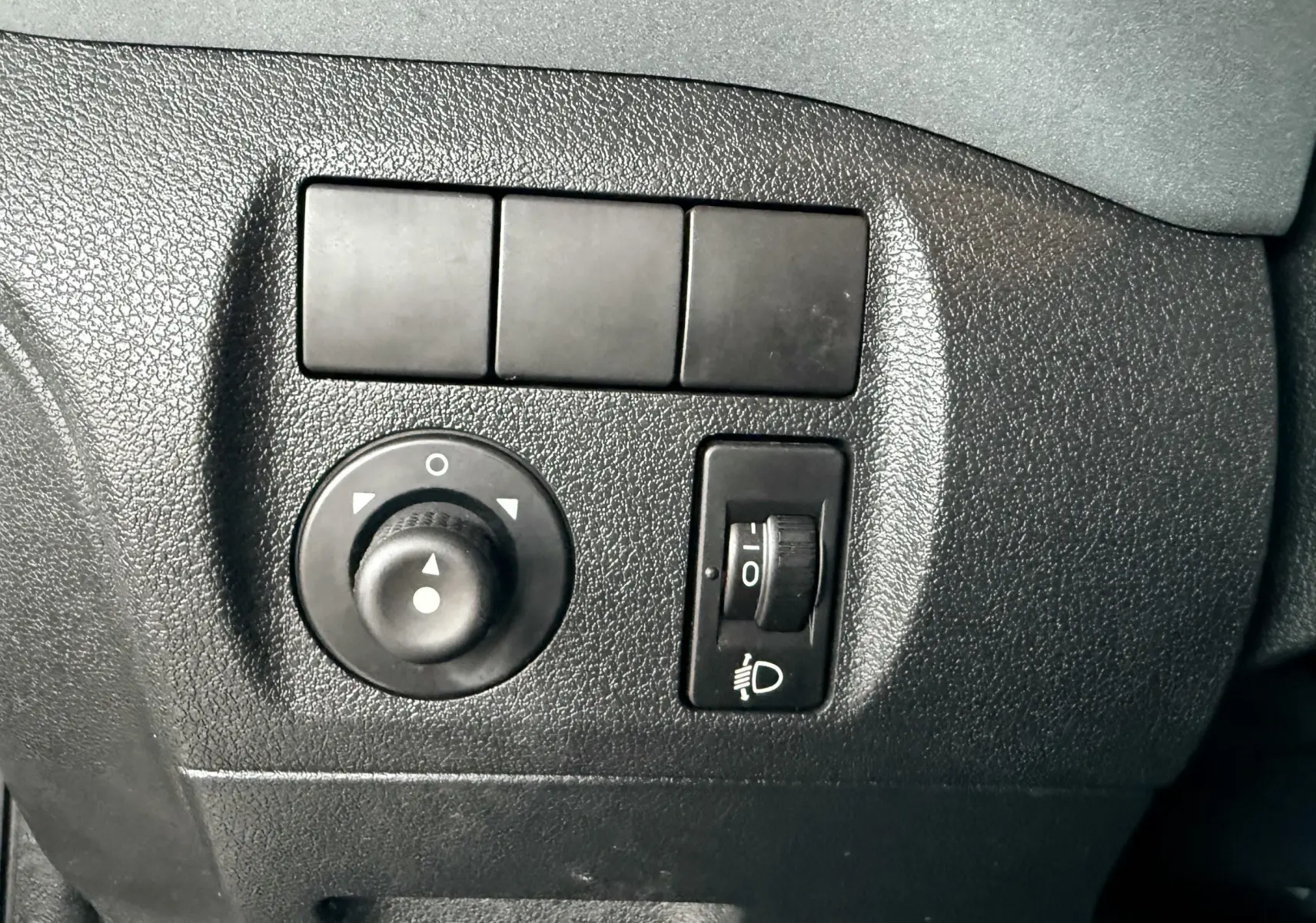Gros plan sur les commandes de réglage des rétroviseurs et des phares du Peugeot Partner Tepee gris, intérieur noir.