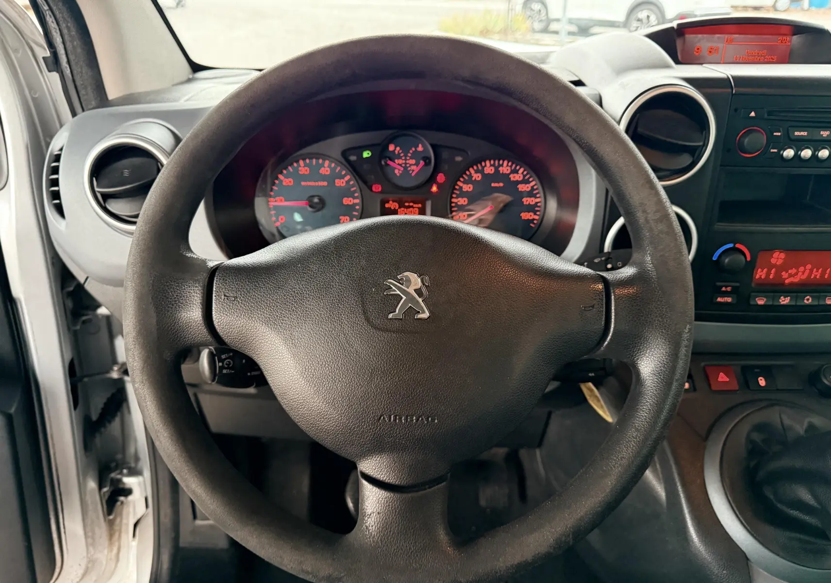 Vue intérieure centrée sur le volant noir de la Peugeot Partner Tepee 2014 avec tableau de bord et console gris foncé.