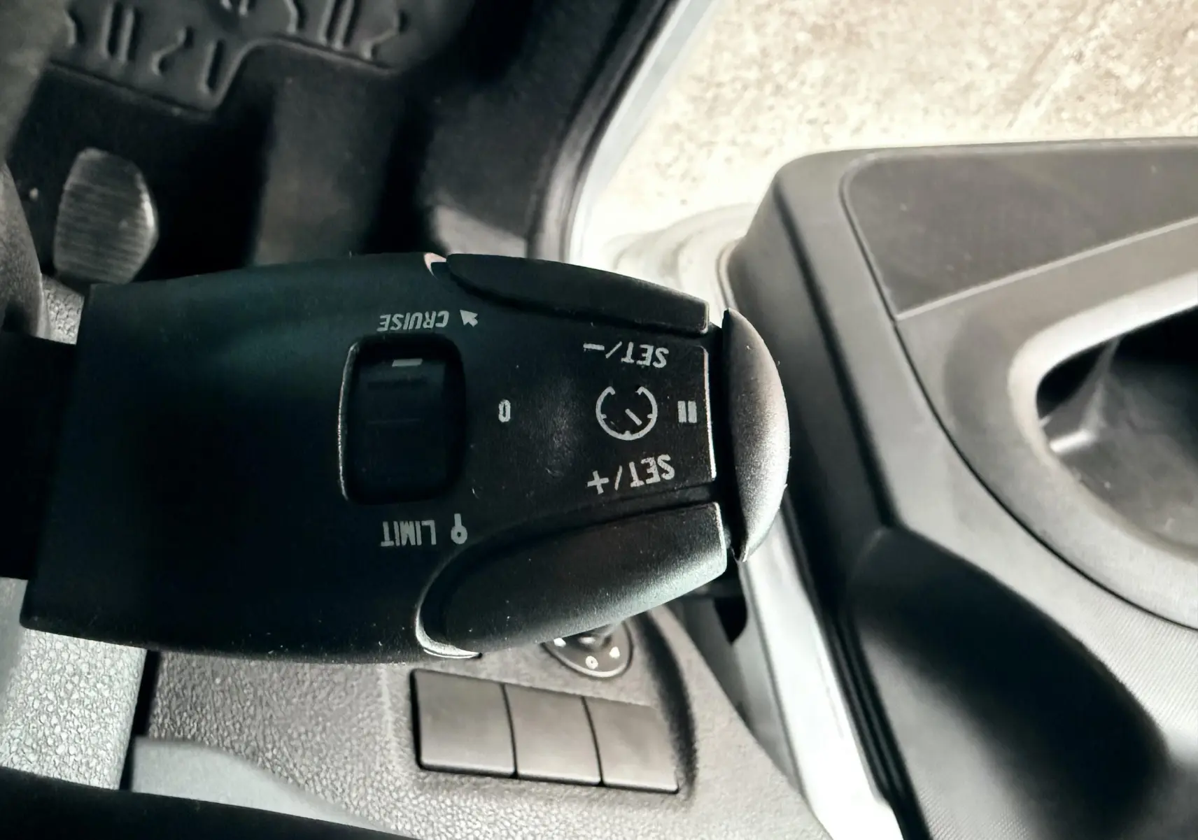Gros plan sur la commande de régulateur de vitesse noire à gauche du volant dans l’habitacle gris du Peugeot Partner Tepee.