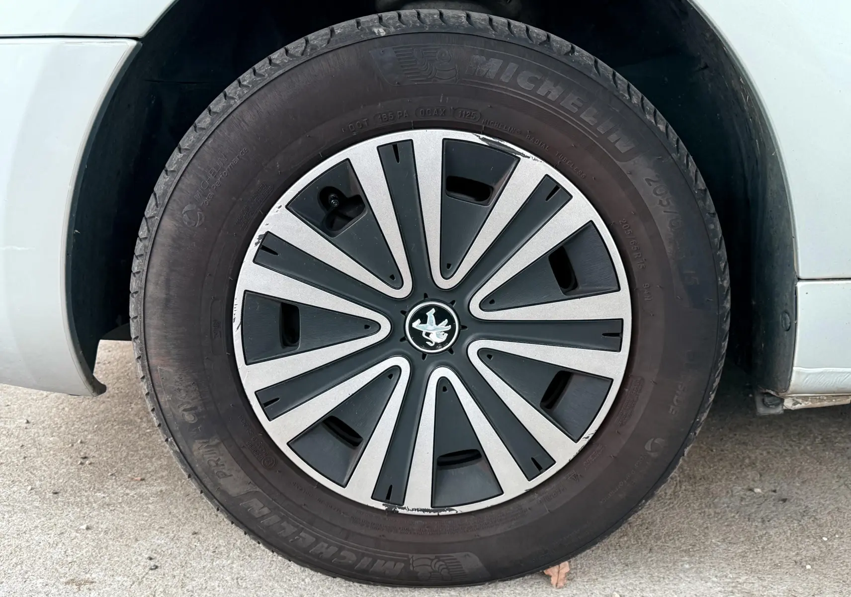 Gros plan sur la roue avant gauche grise d’un Peugeot Partner Tepee avec jante en alliage et logo lion central.