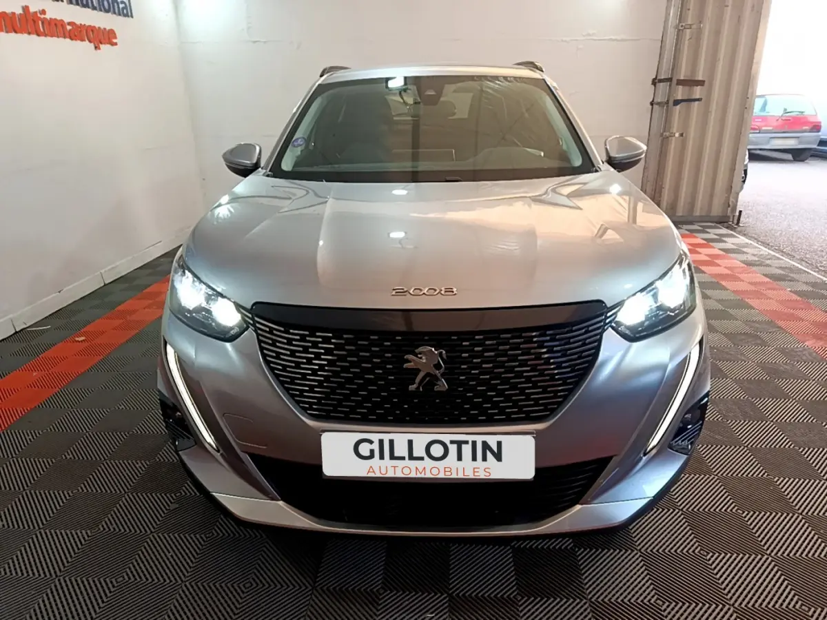 Vue frontale d'un Peugeot 2008 gris clair avec phares LED allumés dans un garage.