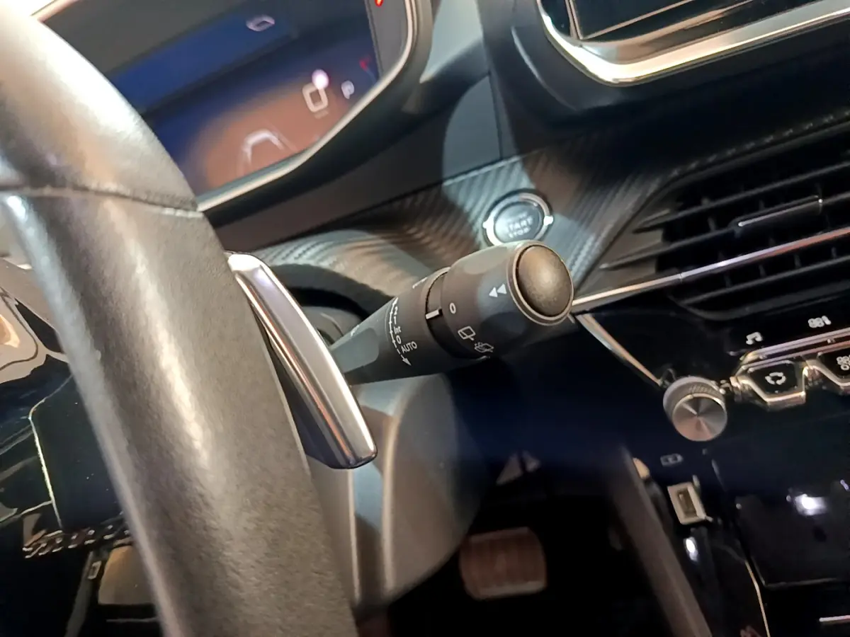 Détail intérieur du Peugeot 2008 2021, vue du volant cuir et commande de phares sur fond de tableau de bord noir.