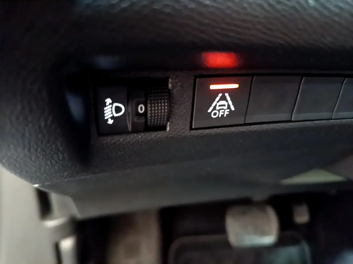 Gros plan sur les commandes de réglage des phares et du système d’aide à la conduite désactivé dans un Peugeot 2008 gris clair.