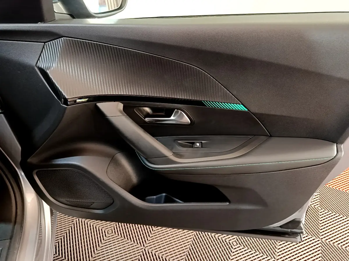 Vue intérieure du panneau de porte avant gauche du Peugeot 2008 gris clair, avec insert imitation carbone et surpiqûres bleues.