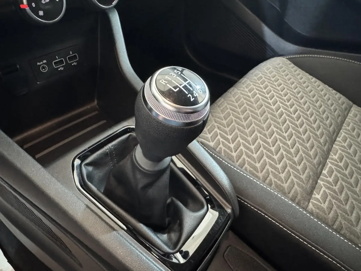 Gros plan sur le levier de vitesses manuel noir et argenté, avec siège tissu gris à motifs à droite dans une Renault Clio blanche.