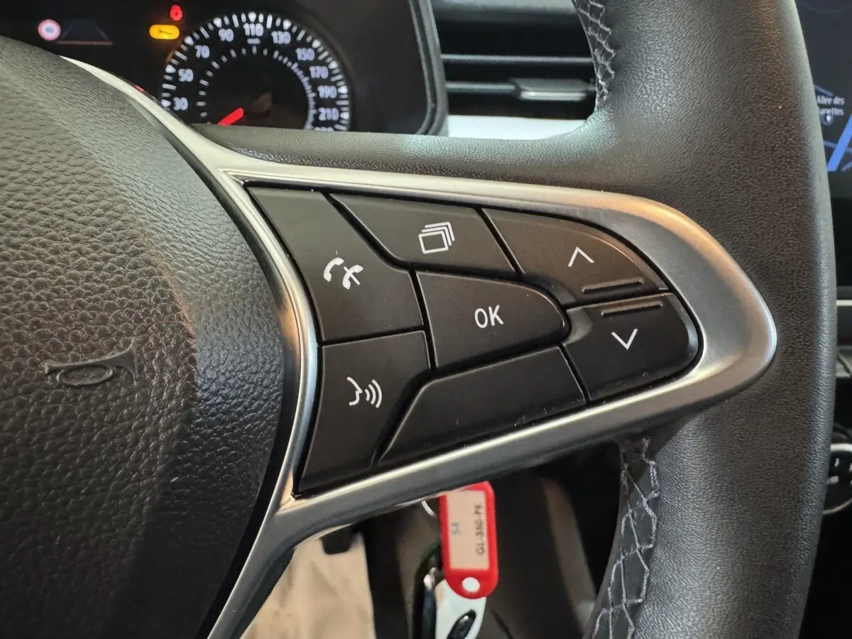 Gros plan sur le volant noir de la Renault Clio Business avec commandes multifonctions et tableau de bord partiellement visible.