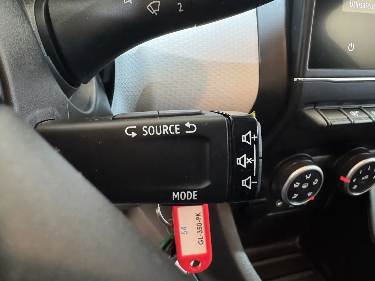 Gros plan sur la commande au volant noir de la Renault Clio Business blanc, avec boutons source et mode visibles.