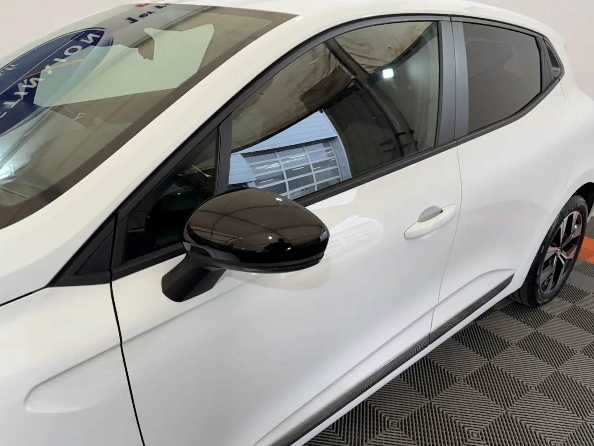 Vue latérale droite rapprochée d'une Renault Clio Business blanche avec rétroviseur noir brillant et jante noire.