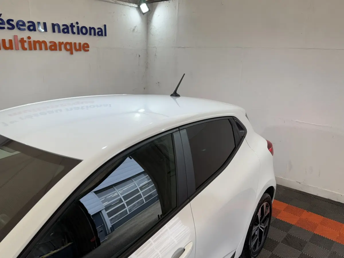 Vue 3/4 arrière droite d'une Renault Clio Business blanche, vitres teintées et jantes noires, dans un garage intérieur.