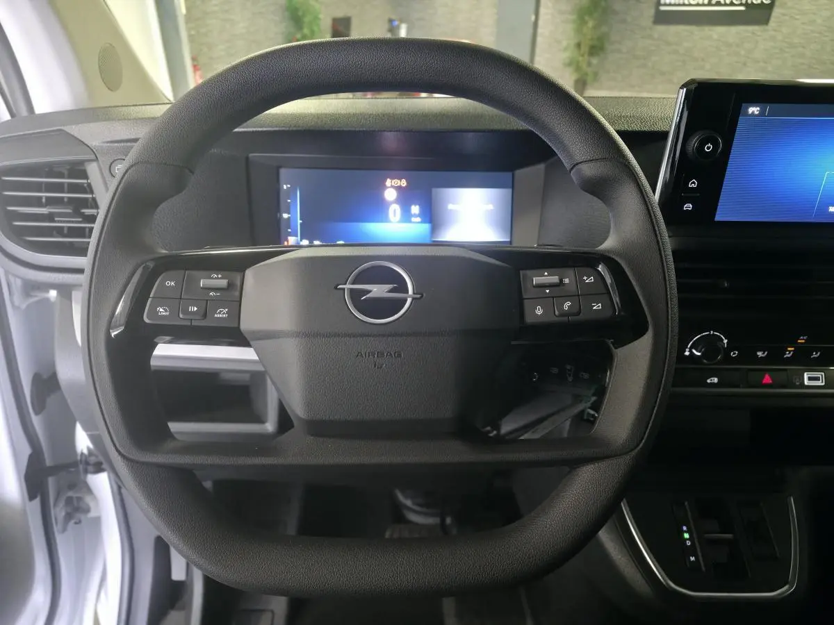Vue frontale du volant noir avec logo Opel, tableau de bord numérique et écran tactile dans l'habitacle blanc du Vivaro 2025.