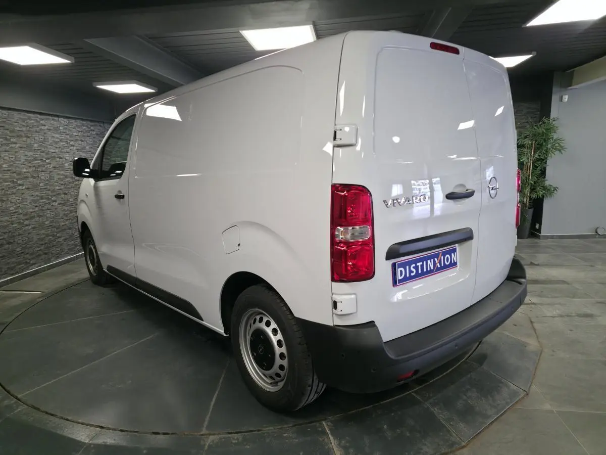 Vue 3/4 arrière droite d’un Opel Vivaro blanc avec portes arrière battantes et jantes tôles grises en intérieur showroom.