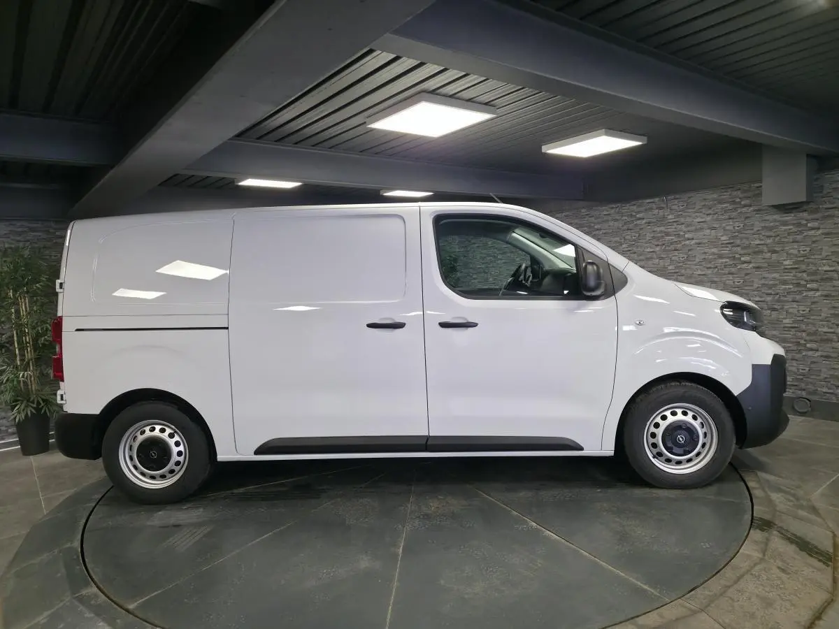 Opel Vivaro blanc en vue de profil côté gauche dans un showroom avec jantes tôles et poignées noires.