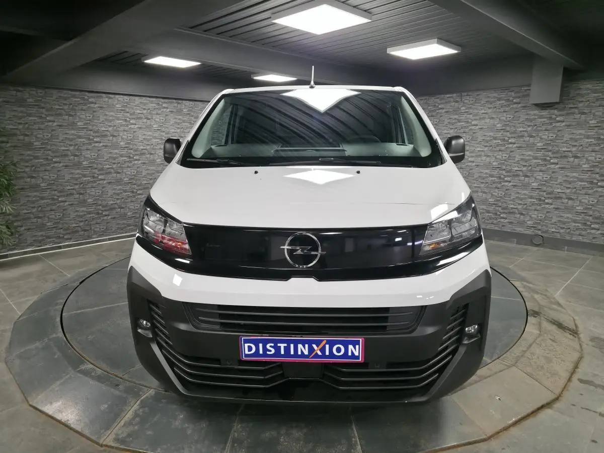 Vue avant d'un Opel Vivaro blanc 2025 avec calandre noire brillante et projecteurs modernes, en intérieur showroom.