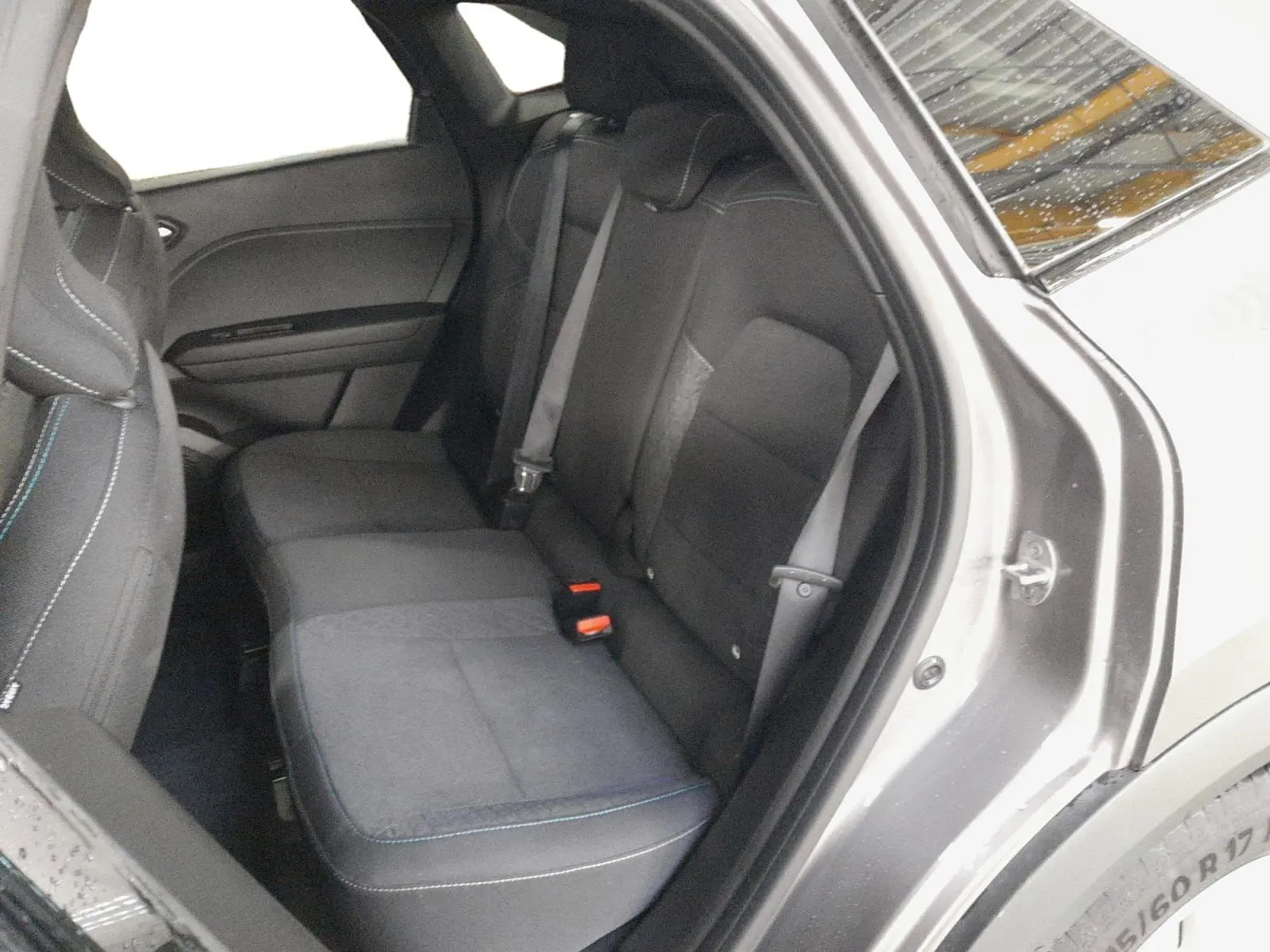 Vue intérieure côté arrière droit du Renault Symbioz gris Cassiopée, montrant les sièges arrière en tissu avec surpiqûres bleues.