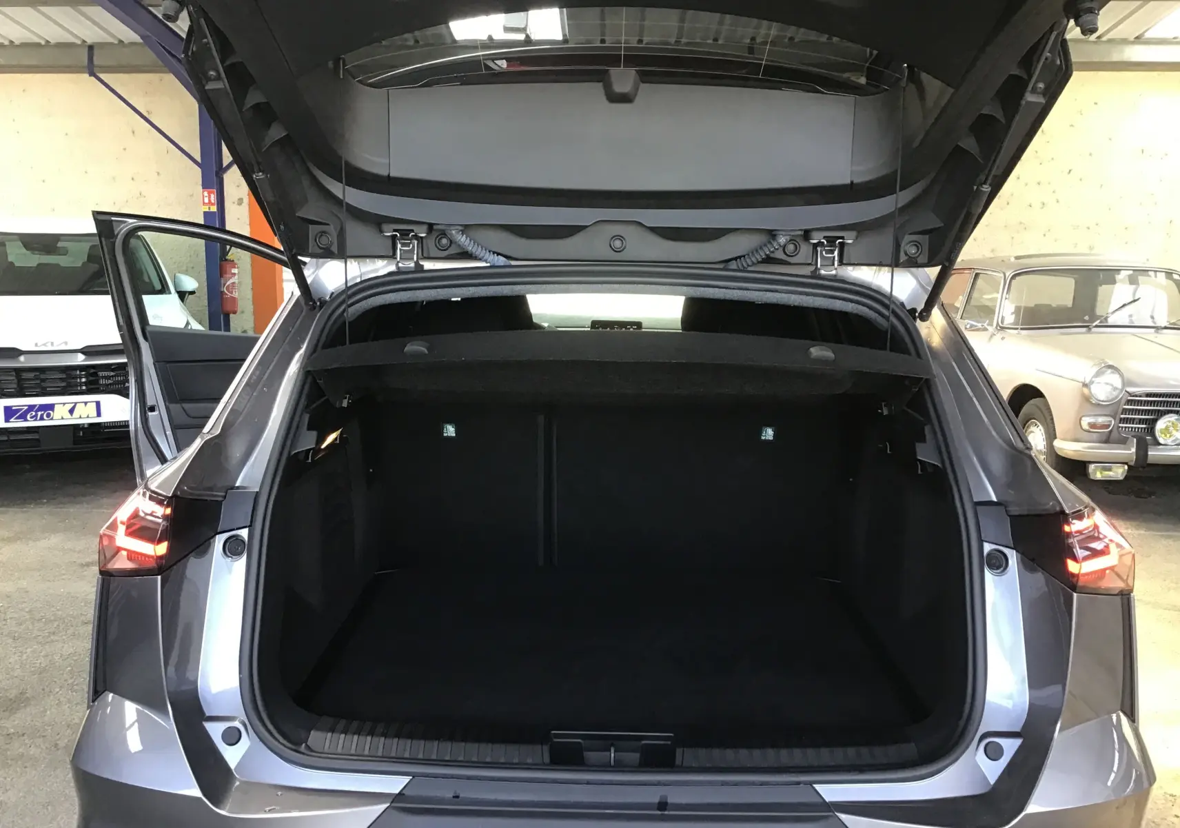 Vue arrière du coffre ouvert du Renault Symbioz gris Cassiopée, mettant en valeur l'espace de chargement et les feux arrière allumés.