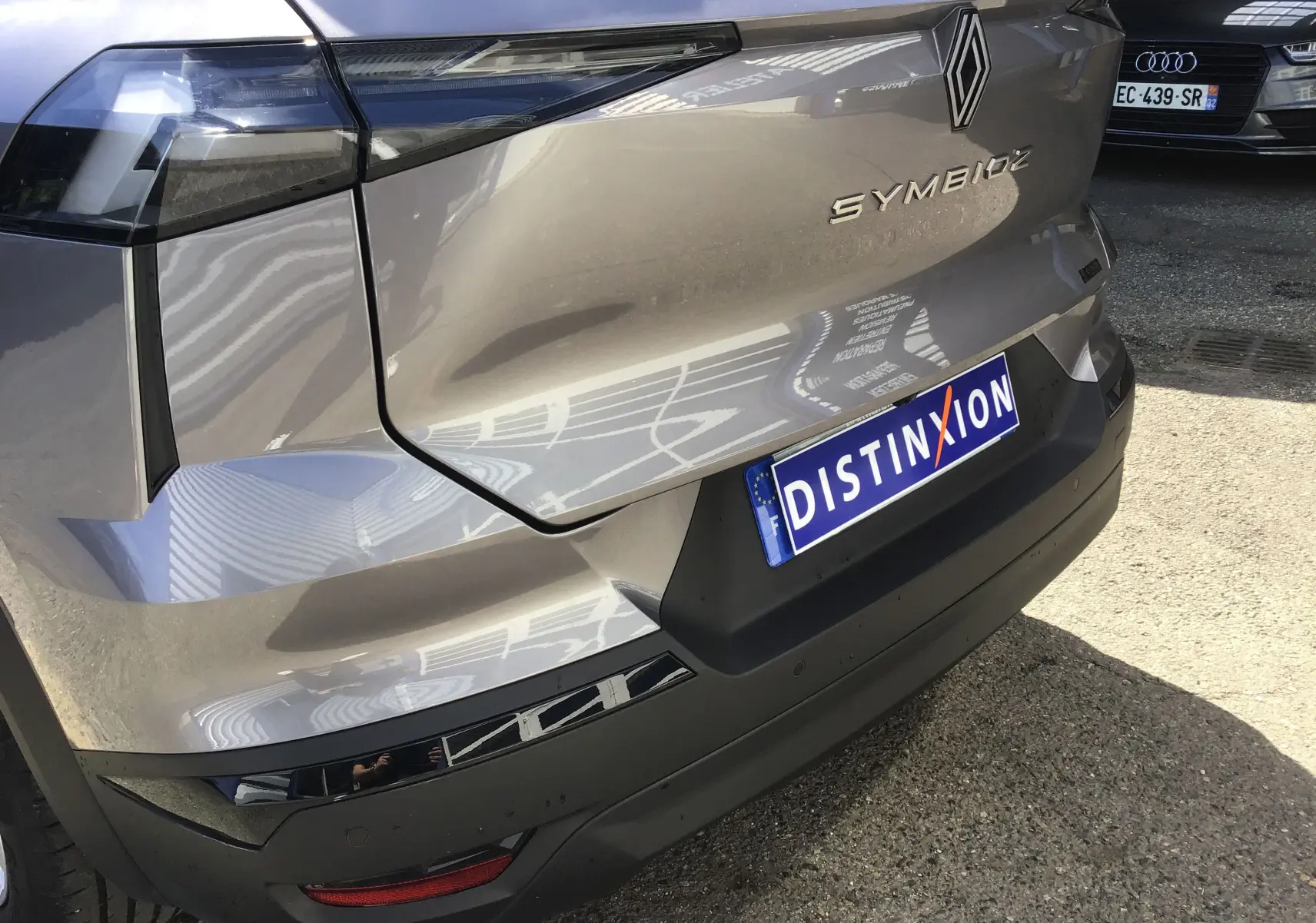 Vue arrière droite du Renault Symbioz gris Cassiopée avec logo et plaque d'immatriculation Distinxion visible.