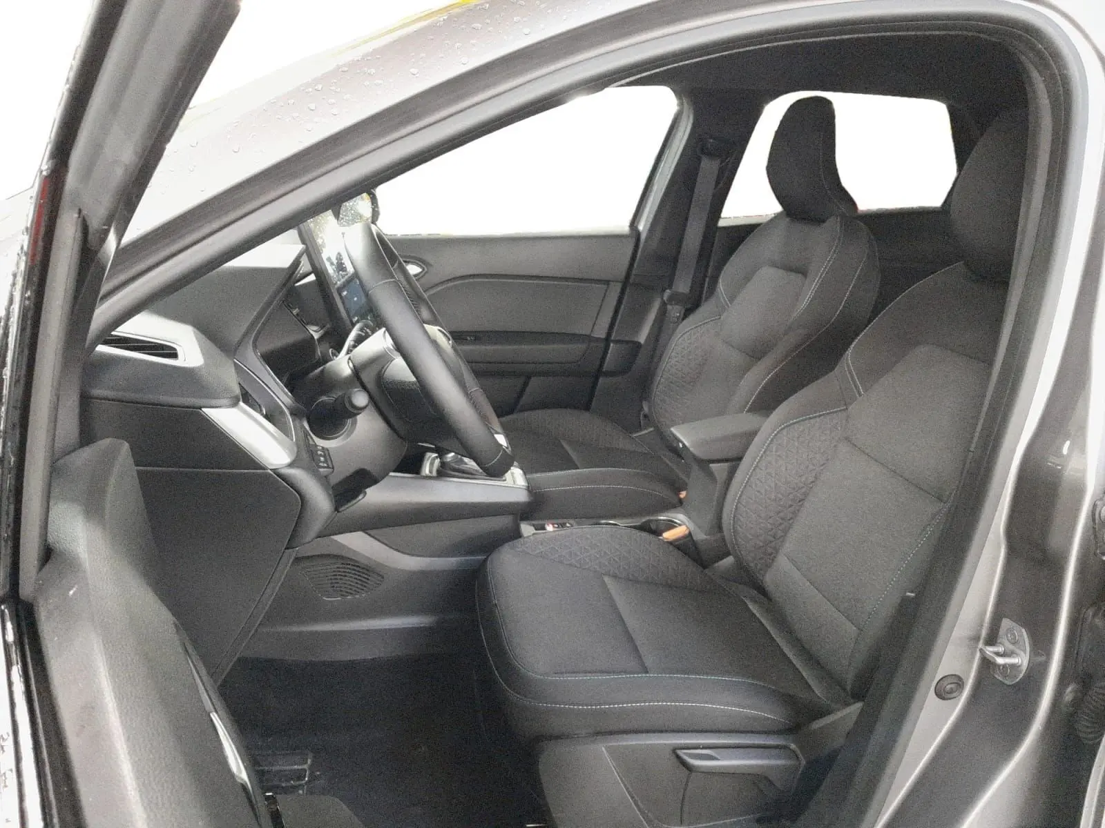 Vue intérieure côté conducteur du Renault Symbioz gris Cassiopée, montrant les sièges avant et le tableau de bord moderne.
