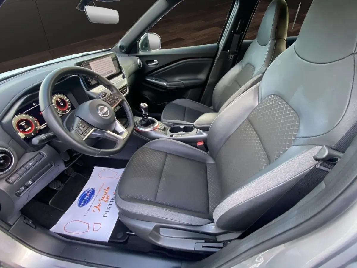 Vue intérieure côté conducteur du Nissan Juke gris clair 2025, montrant sièges tissu et cuir, volant multifonctions et écran tactile.