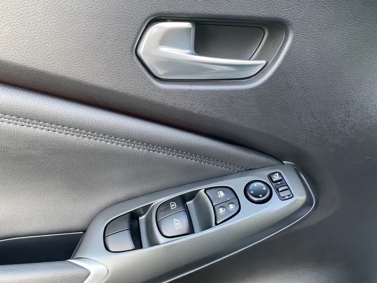 Gros plan sur la commande de lève-vitres et rétroviseurs côté conducteur, garniture intérieure noire du Nissan Juke 2025.
