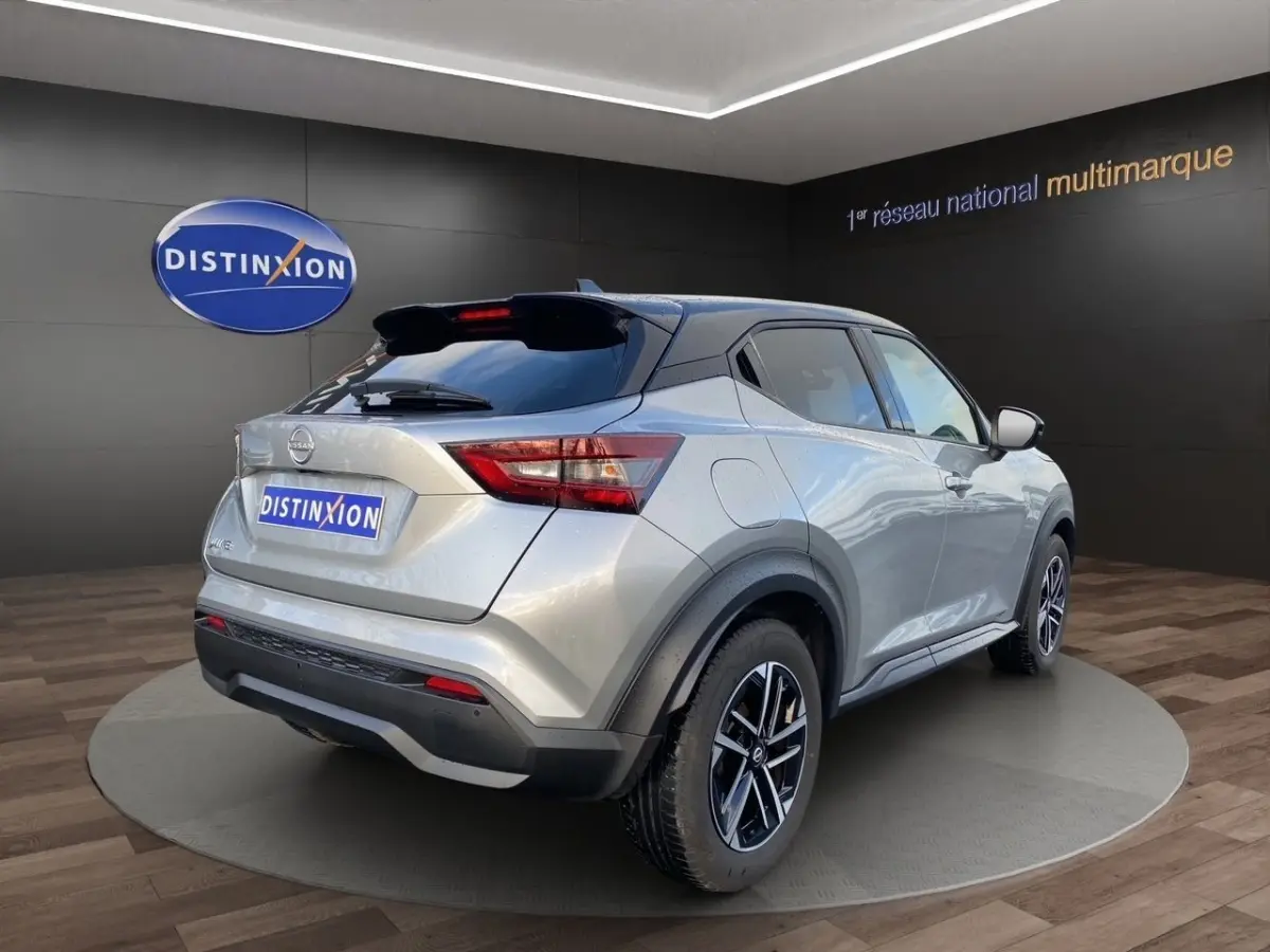 Nissan Juke gris clair vue 3/4 arrière droit, avec jantes alliage et toit noir contrasté en showroom.