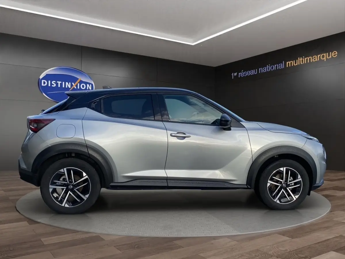 Profil droit du Nissan Juke gris clair 2025 avec jantes alliage et toit noir contrasté en showroom.